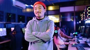 Smiling Chinese male gamer with crossed arms in gaming club.